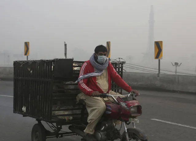 A tri-wheeler passes by Minar-e-Pakistan, the Pakistani monument, while smog envelopes the area in Lahore, Pakistan, Sunday, November 5, 2017. Smog has enveloped much of Pakistan and neighboring India, causing highway accidents and respiratory problems, and forcing many residents to stay home, officials said. (Photo by K.M. Chaudary/AP Photo)