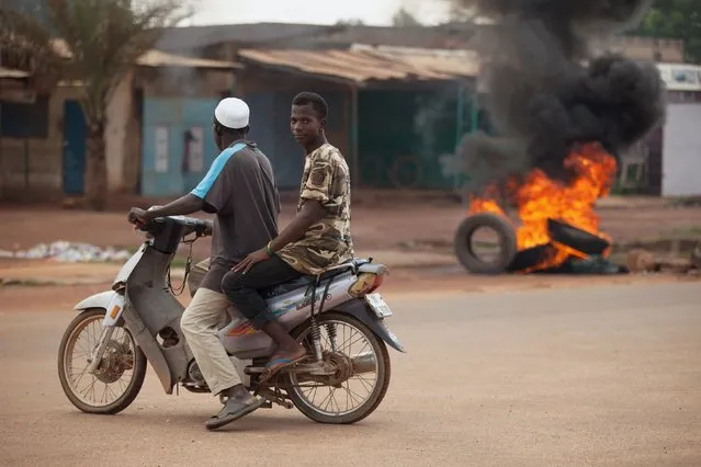 Men ride a motorcycle past a burning barricade set up by anti-coup protesters in Ouagadougou, Burkina Faso, September 21, 2015. Regional mediators seeking to peacefully roll back a military coup in Burkina Faso said they negotiated a draft deal on Sunday to end the crisis though they failed to secure the immediate restoration of civilian rule. (Photo by Joe Penney/Reuters)