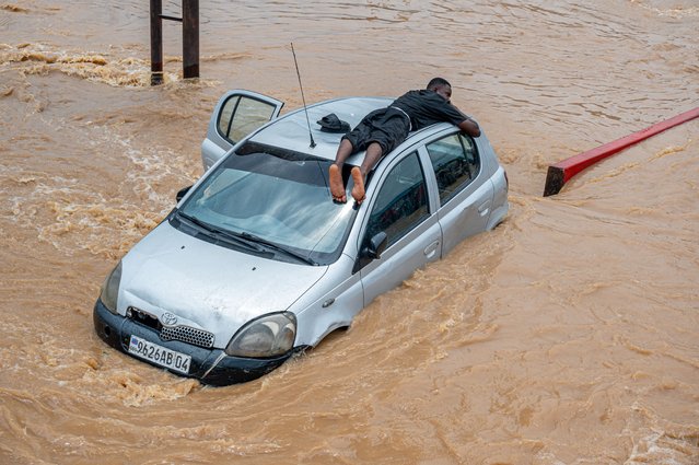 A man lies on top of a car for safety as floodwaters inundate a road following heavy rains in the Ndjili district of Kinshasa on April 6, 2025. Heavy downpours in the Democratic Republic of Congo's capital Kinshasa have left around 30 people dead while wrecking havoc in the central African megacity, an official told AFP on April 6, 2025. After the rain poured down overnight from Friday to Saturday, the rising water levels devastated several outlying and impoverished suburbs of the metropolis of some 17 million people. (Photo by Hardy Bope/AFP Photo)