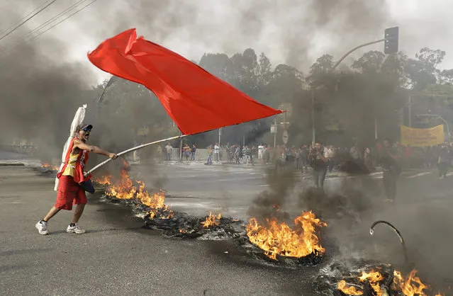 A demonstrator waves a red banner next to a burning barricade during a protest against Brazil's acting President Michel Temer, in Sao Paulo, Brazil, Tuesday, August 30, 2016. (Photo by Andre Penner/AP Photo)
