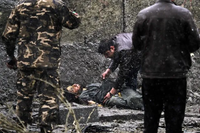 Afghan security and intelligence agents check a man who was killed by suicide bombers riding in minivans that struck the headquarters of the Afghan intelligence agency in Kabul, January 16, 2013.The Taliban claimed responsibility for the attack killed several people and injured more than 30. (Photo by Ahmad Jamshid/Associated Press)