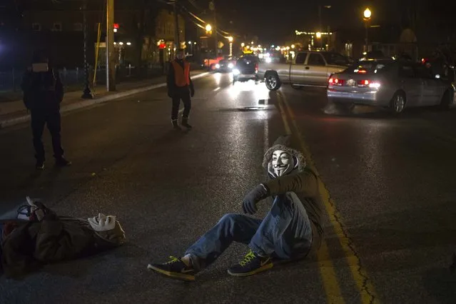 Activists, wearing Guy Fawkes masks, block traffic while protesting the shooting of Michael Brown, outside the Ferguson Police Station in Missouri, November 19, 2014. Residents of Ferguson prepared on Wednesday for a grand jury report expected soon on the fatal August shooting of Brown, an event that laid bare long-simmering racial tensions in the St. Louis suburb. (Photo by Adrees Latif/Reuters)