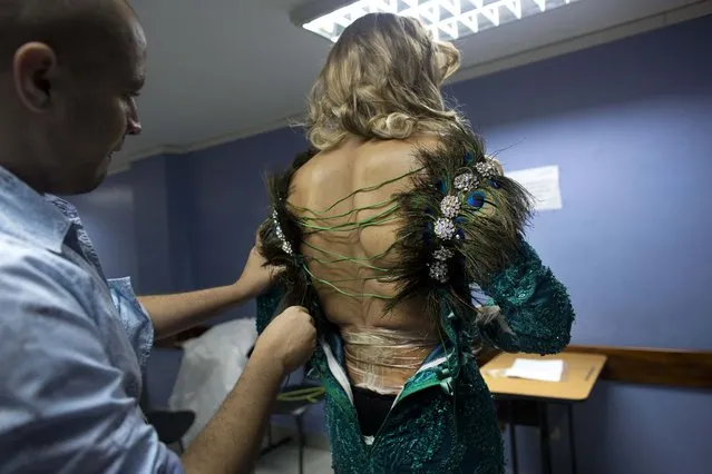 In this October 18, 2015 photo, a contestant is helped with his dress backstage at the ninth annual Miss Gay Venezuela beauty pageant in Caracas, Venezuela. After painstaking preparation, contestants wearing 1950s-style cat eye makeup, pink lips and blonde pin curls performed song and dance numbers and strutted their stuff in sequined dresses created by some of Venezuela's top designers. (Photo by Ariana Cubillos/AP Photo)