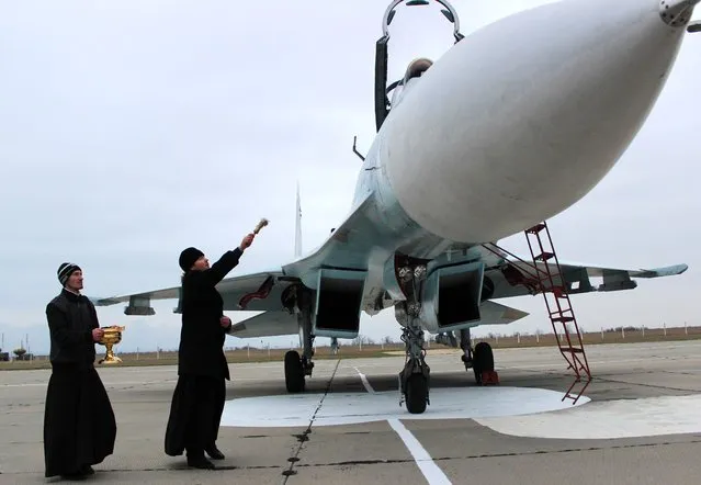 A Russian orthodox priest blesses a SU-27 SM fighter jet on the airfield of Belbek military airport outside Sevastopol on November 26, 2014. Crimean military air forces were reinforced by ten Russian SU-27 SM and four SU-30 fighter jets today. NATO's top military commander warned Wednesday that Russia's “militarisation” of the annexed Crimea peninsula could be used by Moscow to exert control across the whole Black Sea region. (Photo by Yuri Lashov/AFP Photo)