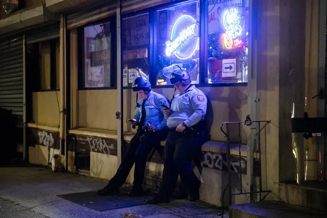 Police officers look at their mobile phones after the city imposed a 9pm curfew in Philadelphia, October 28, 2020, following two nights of protesting and unrest after the fatal shooting of Walter Wallace Jr. by police. Officials in the US city of Philadelphia announced a nighttime curfew on October 28 following two nights of unrest over the latest police killing of a Black man whose family said suffered from mental health issues. Thousands of people have taken to Philadelphia's streets, with looting and violence breaking out, since police on Monday shot dead 27-year-old Walter Wallace, who was carrying a knife. (Photo by Gabriella Audi/AFP Photo)