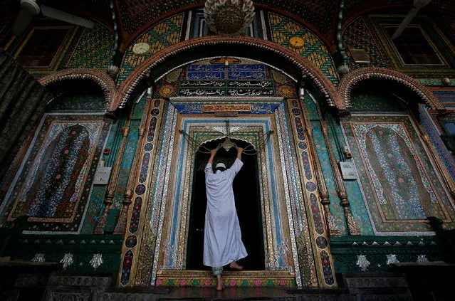A Muslim man touches an ornament, engraved with verses from the Koran, tied to a chain at the shrine of Mir Syed Ali Hamdani, a Sufi saint, during the holy month of Ramadan in Srinagar May 24, 2018. (Photo by Danish Ismail/Reuters)