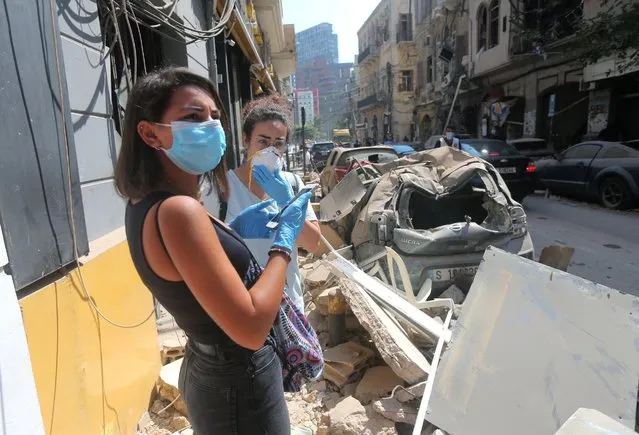 Young Lebanese women wearing protective masks and gloves against the coronavirus pandemic, stand on August 5, 2020 amid the rubble in Beirut's Gimmayzeh commercial district which was heavily damaged by the previous day's powerful explosion that tore through Lebanon's capital, resulting from the ignition of a huge depot of ammonium nitrate at the city's main port. Rescuers searched for survivors in Beirut after a cataclysmic explosion at the port sowed devastation across entire neighbourhoods, killing more than 100 people, wounding thousands and plunging Lebanon deeper into crisis. The blast, which appeared to have been caused by a fire igniting 2,750 tonnes of ammonium nitrate left unsecured in a warehouse, was felt as far away as Cyprus, some 150 miles (240 kilometres) to the northwest. (Photo by AFP Photo/Stringer)