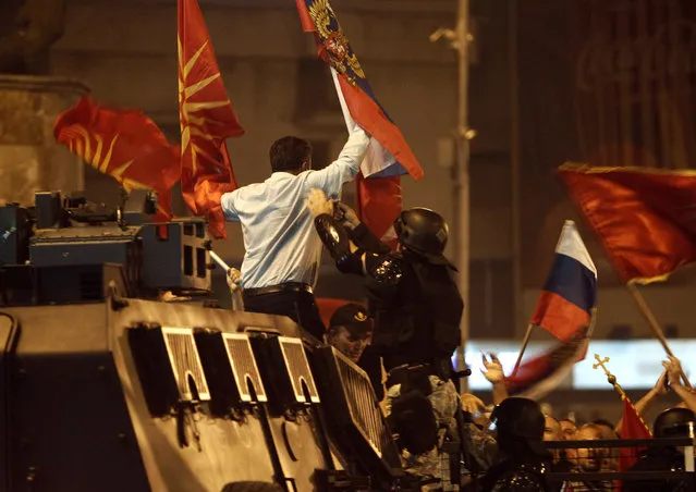A police officer tries to grab a protester waving former Macedonian and Russian flags atop of a police vehicle during a protest of opponents of the deal between Greece and Macedonia on the latter country's new name “North Macedonia”, outside the parliament in Skopje, Macedonia, Sunday, June 17, 2018. The preliminary deal signed by the two countries' foreign ministers in the Prespes Lakes area, Greece, launches a long process that will last several months. If successful, it will end a decades-long dispute between neighbors Greece and Macedonia, which will be renamed North Macedonia. (Photo by Boris Grdanoski/AP Photo)
