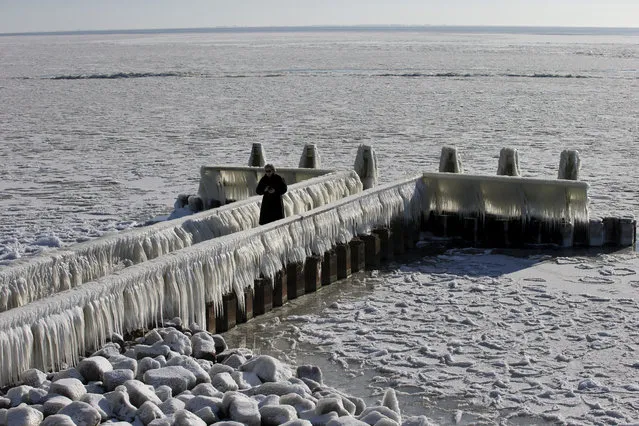 A woman takes pictures of icicles on a jetty at the Afsluitdijk, a dike separating IJsselmeer inland sea, and the Wadden Sea, Netherlands, Thursday, February 11, 2021. The deep freeze gripping parts of Europe served up fun and frustration with heavy snow cutting power to some 37,000 homes in central Slovakia. (Photo by Peter Dejong/AP Photo)
