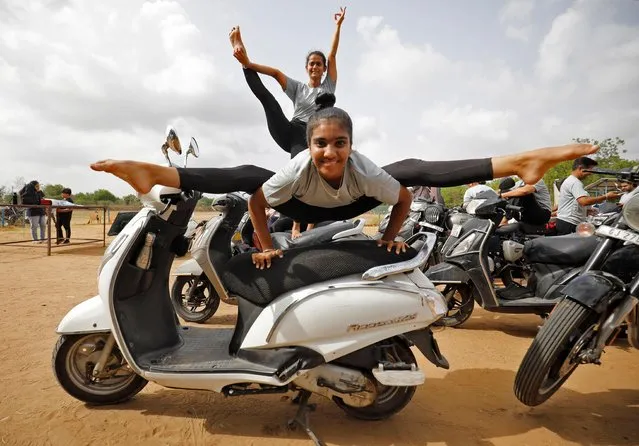 Girls perform yoga on their scooters at a park on International Yoga Day in Ahmedabad, India, June 21, 2022. (Photo by Amit Dave/Reuters)