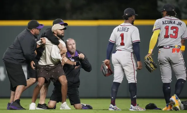 Field guards hold onto a fan as he tries to reach Atlanta Braves right fielder Ronald Acuna Jr., right, while second baseman Ozzie Albies (1) looks on in the seventh inning of a baseball game against the Colorado Rockies, Monday, August 28, 2023, in Denver. (Photo by David Zalubowski/AP Photo)