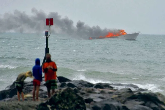 People stand on the shoreline as a tourist boat carrying 60 people burns out at sea off the coast of Whakatane, New Zealand, Monday, January 18, 2016. All 60 people forced overboard after the tourist boat caught fire Monday have been rescued, according to authorities. (Photo by Whakatane Beacon via AP Photo)