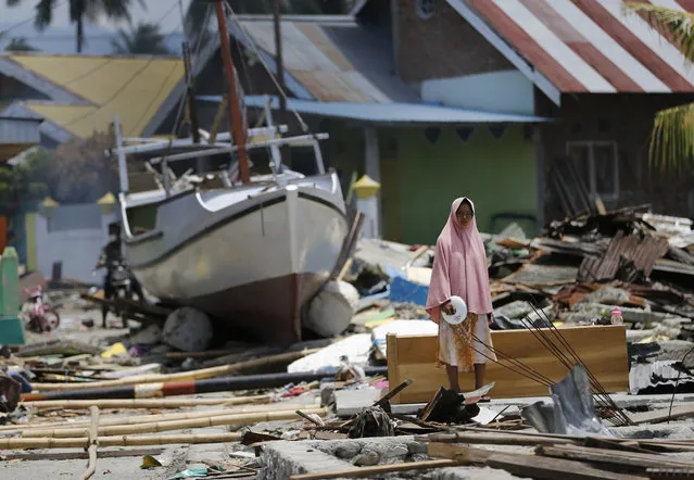 A woman stands in the rubble of houses as a boat swept ashore by tsunami rests on the ground in the background in Wani village on the outskirt of Palu, Central Sulawesi, Indonesia, Wednesday, October 10, 2018. A 7.5 magnitude earthquake rocked Central Sulawesi province on Sept. 28, triggering a tsunami and mudslides that killed a large number of people and displaced tens of thousands of others. (Photo by Dita Alangkara/AP Photo)