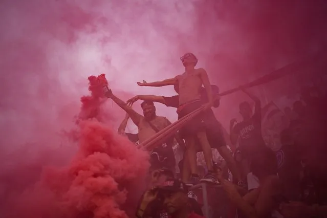 Members of the Caracas FC fan club, who call themselves The Red Demons, light red smoke flares as they cheer for their team during the derby soccer match against Deportivo Tachira at Estadio Olimpico in Caracas, Venezuela, Sunday, July 23, 2023. (Photo by Matias Delacroix/AP Photo)