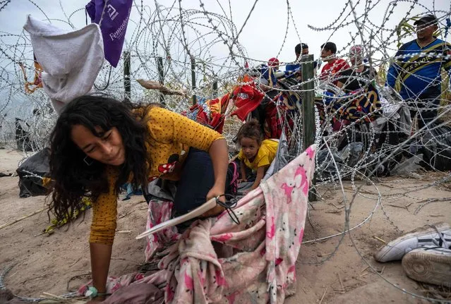 Migrants from Venezuela crawl through a hole in the razor wire to cross into Eagle Pass, Texas on September 25, 2023. Dozens of migrants arrived at the US-Mexico border on September 22, 2023, hoping to be allowed into the United States, with US border forces reporting 1.8 million encounters with migrants in the last 12 months. (Photo by Andrew Caballero-Reynolds/AFP Photo)