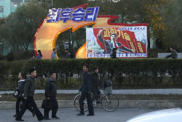 In this Saturday, October 27, 2018 photo, people walk past a propaganda banner that reads “Final victory!  With science and technology we build our economic power” in Pyongyang, North Korea. (Photo by Dita Alangkara/AP Photo)