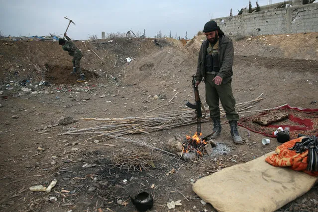 A rebel fighter of Jaysh al-Islam warms himself near a fire, on al-Rayhan village front near the rebel held besieged Douma neighbourhood of Damascus, Syria January 2, 2017. (Photo by Bassam Khabieh/Reuters)