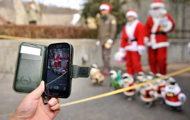 A visitor takes a photo of penguins (bottom R) dressed in costumes as they are paraded at an amusement park for a promotional event ahead of Christmas in Yongin, south of Seoul, on December 18, 2013. (Photo by Woohae Cho/AFP Photo)