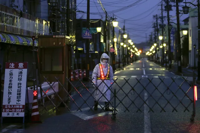 A security guard stands guard on one of the totally empty main streets at dusk in rainy Namie, a town north of Tokyo Electric Power Company's Fukushima Daiichi Nuclear Power Plant, Fukushima Prefecture, northern Japan, 09 March 2016. Japan will mark the fifth anniversary of the earthquake and tsunami on 11 March 2016. According to Japan's National Police Agency, a total of 15,894 people were killed in the disaster and 2,562 are still missing as of February 2016. A group of 174,471 people are still living in shelters, according to records. (Photo by Kimimasa Mayama/EPA)