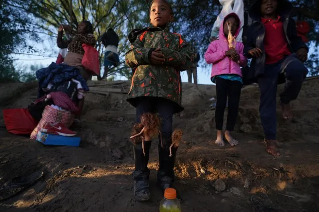 A girl with Barbie dolls stuffed in her boots waits with others to cross the Rio Grande river with their parents as they stand on the bank of the Rio Grande river in Ciudad Acuna, Mexico, at dawn Thursday, September 23, 2021, across the border from Del Rio, Texas. (Photo by Fernando Llano/AP Photo)