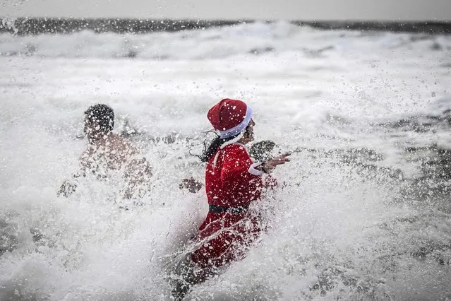 A woman in a Santa Claus costume celebrates New Year's Day taking the traditional first dip of the year in the frigid waters of the Atlantic ocean, at Carcavelos beach in Oeiras, Lisbon district, on January 1, 2023. (Photo by Patricia de Melo/AFP Photo)