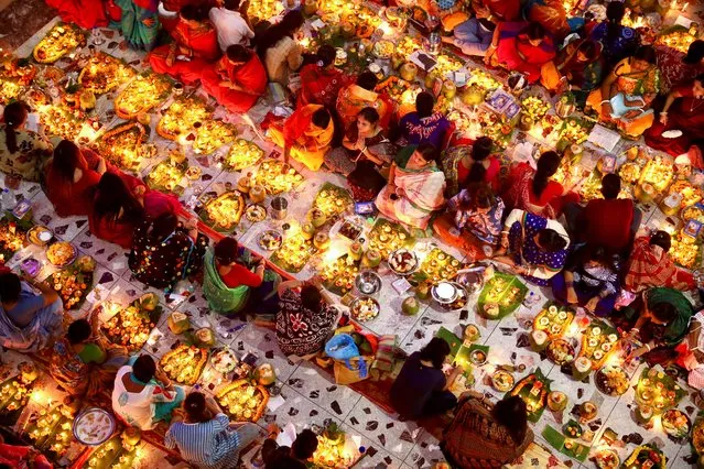 Hindu devotees sit together on the floor of a temple with oil lamps, praying to Lokenath Brahmachari, a Hindu saint, as they observe Rakher Upabash, in Dhaka, Bangladesh, November 9, 2021. (Photo by Mohammad Ponir Hossain/Reuters)