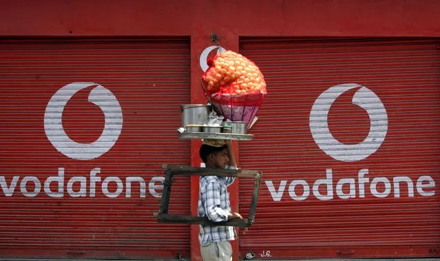 A vendor selling “paani puri”, a traditional Indian snack, walks past closed shops displaying an advertisement for Vodafone in Jammu May 22, 2012. (Photo by Mukesh Gupta/Reuters)