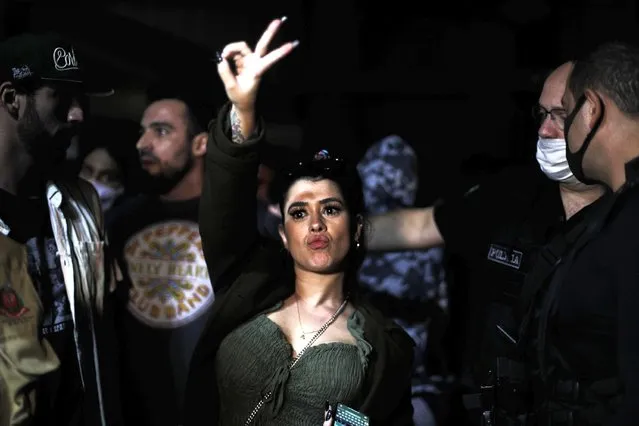 A woman flashes a V sign as police break up a social gathering during an operation against illegal and clandestine gatherings that authorities believe are partly responsible for fueling the spread of COVID-19, at a party hall in Sao Paulo, Brazil, early Saturday, April 17, 2021. (Photo by Marcelo Chello/AP Photo)
