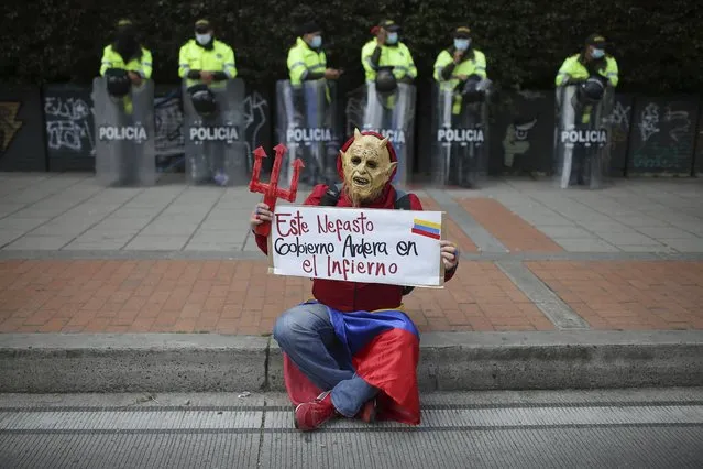 A man in a devil costume holds the Spanish sign “This disastrous government will burn in hell” in front of police standing on the sidelines of an anti-government march in Bogota, Colombia, Wednesday, May 19, 2021. Colombians have taken to the streets for weeks across the country after the government proposed tax increases on public services, fuel, wages and pensions. (Photo by Ivan Valencia/AP Photo)