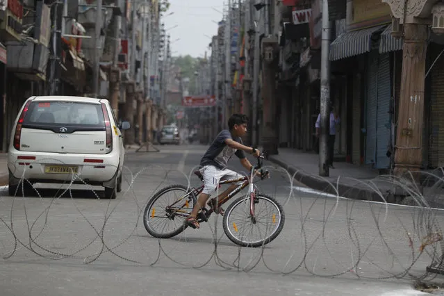 An Indian boy rides a bicycle past a barbed wire erected as part of security restrictions in Jammu, India, Tuesday, Aug.6, 2019. India's lower house of Parliament was set to ratify a bill Tuesday that would downgrade the governance of India-administered, Muslim-majority Kashmir amid an indefinite security lockdown in the disputed Himalayan region. The Hindu nationalist-led government of Prime Minister Narendra Modi moved the “Jammu and Kashmir Reorganization Bill” for a vote by the Lok Sahba a day after the measure was introduced alongside a presidential order dissolving a constitutional provision that gave Kashmiris exclusive, hereditary rights. (Photo by Channi Anand/AP Photo)