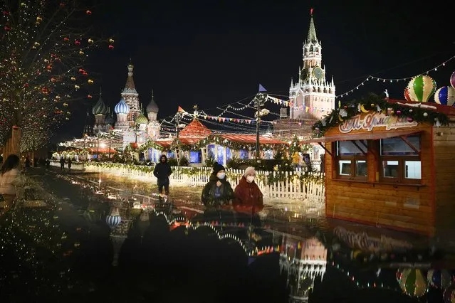 People walk past a Market set up in Red Square with the St. Basil's Cathedral, left, and the Spasskaya Tower, right, in Moscow, Russia, late Monday, February 14, 2022. (Photo by Alexander Zemlianichenko/AP Photo)