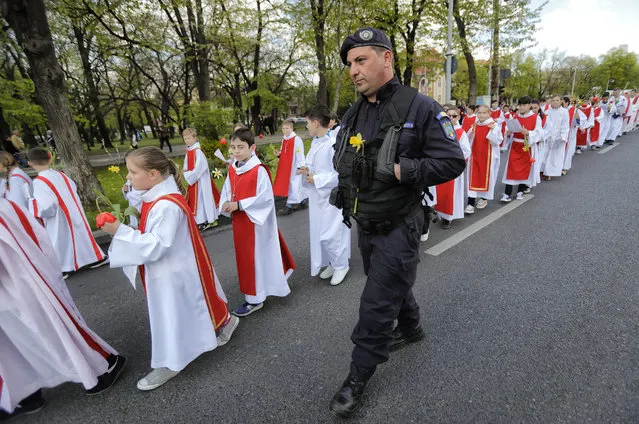 In this Sunday, April 9, 2017, picture a gendarme with a flowers attached to his uniform walks next to Catholic children taking part in a Palm Sunday procession in Bucharest, Romania. (Photo by Vadim Ghirda/AP Photo)