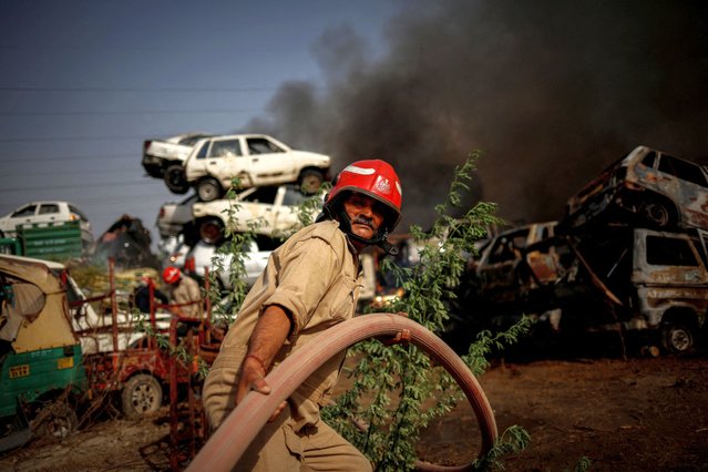 Firefighter Sijender Kumar, 54, pulls a water pipe as he and others try to extinguish a fire that broke out at a car scrapyard in New Delhi, India May 30, 2024. Over a dozen firefighters and officers in Delhi were interviewed by Reuters, many of whom described working in “doubly” strenuous conditions of extreme heat and numerous fires. Shifts for firefighters are 24 hours long, followed by a day of rest. Senior officers work three full-day shifts at a time and then take a day off. (Photo by Adnan Abidi/Reuters)