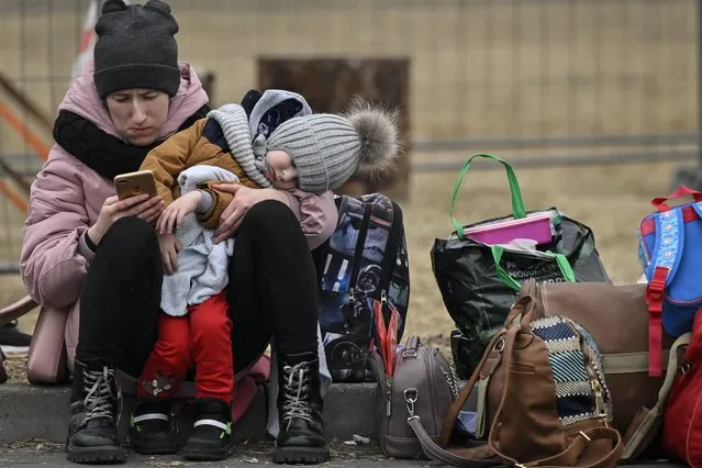 A woman with her child checks her mobile phone as she waits for relocation outside the main shelter and relocation center in Przemysl, southeastern Poland on March 16, 2022. More than three million people have fled Ukraine since the start of the invasion, the UN migration agency IOM says. Around half are minors, says the UN children's agency. The UN refugee agency, UNHCR, says 1.8 million people have fled to Poland. (Photo by Louisa Gouliamaki/AFP Photo)
