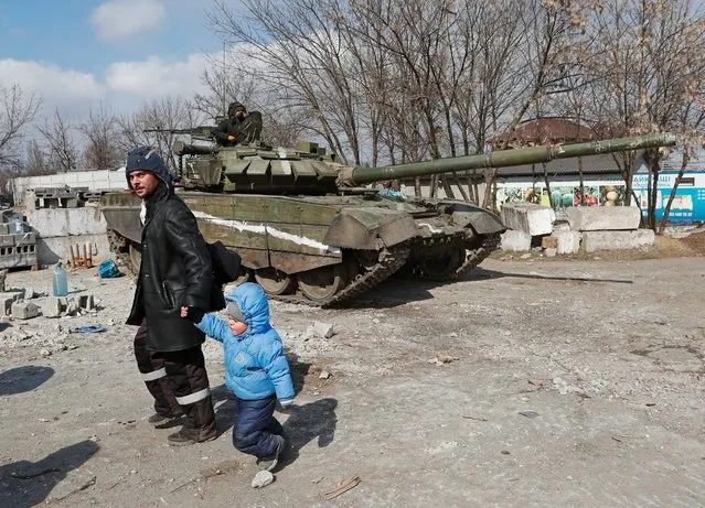A local resident walks with a child past a tank of pro-Russian troops during Ukraine-Russia conflict in the besieged southern port city of Mariupol, Ukraine on March 18, 2022. (Photo by Alexander Ermochenko/Reuters)