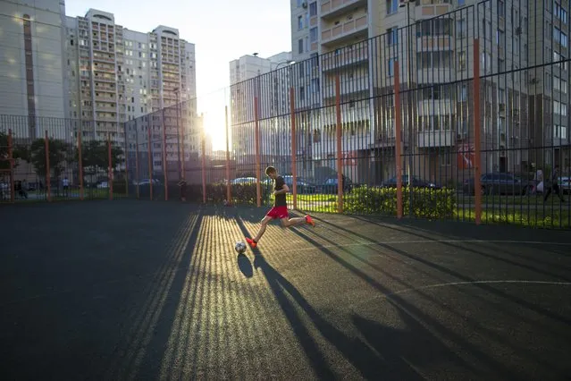 In this July 2, 2015 photo, a teenager plays soccer in the last rays of the setting sun at a playground in Moscow, Russia. While the Brazilians learn to play on the streets or the beach, Russian children have the “dvor”, the yard space between towering apartments blocks. Yard football is a national tradition, and the asphalt pitches are often the first step in the careers of future stars of the Russian national team. (Photo by Alexander Zemlianichenko/AP Photo)