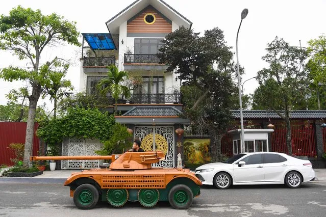 Truong Van Dao rides past a house in a wooden tank made from the conversion of an old minibus in a residential area in Bac Ninh province on March 28, 2022. A Vietnamese father spent hundreds of hours, investing thousands, to convert an old van into a wooden tank for his son – an unusual hobby in a country once ravaged by war. (Photo by Nhac Nguyen/AFP Photo)