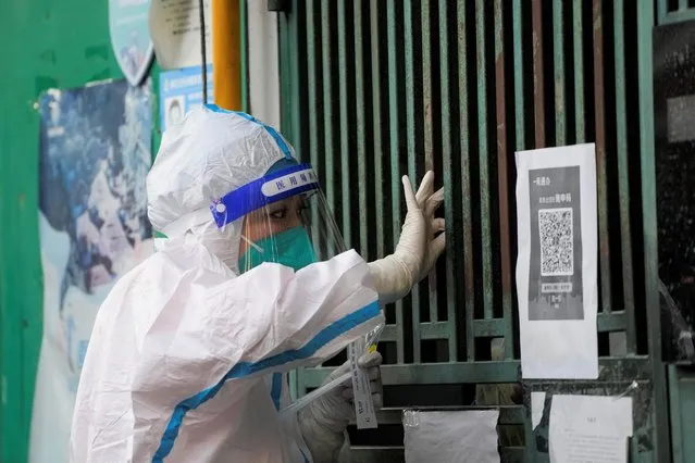 A medical worker in a protective suit collects a swab sample from a resident for nucleic acid testing, outside a closed entrance of a building during lockdown, amid the coronavirus disease (COVID-19) pandemic, in Shanghai, China on May 5, 2022. (Photo by Aly Song/Reuters)