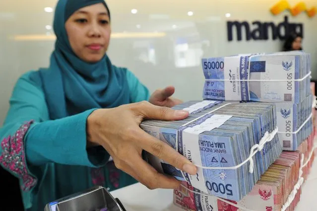 A teller at a Bank Mandiri branch handles Indonesian Rupiah currency during a transaction in Jakarta July 20, 2015 in this photo taken by Antara Foto. The Indonesian rupiah hit a fresh 17-year low on July 23, 2015, as solid U.S. housing data added to expectations the Federal Reserve with hike interest rates as soon as September. (Photo by Wahyu Putro/Reuters/Antara Foto)