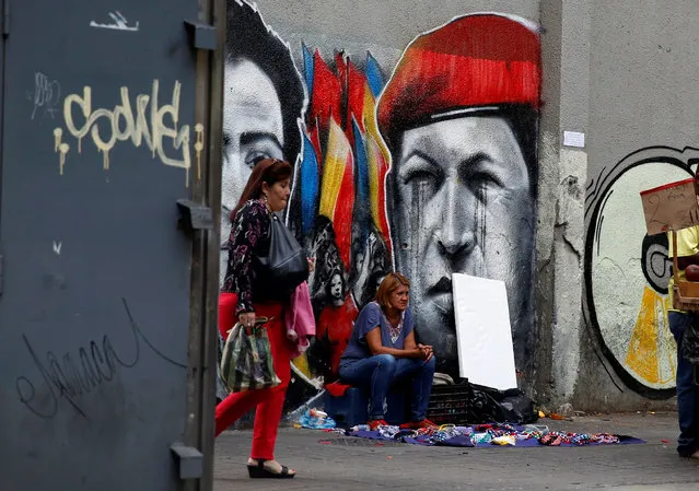 A street vendor sits next to graffiti depicting Venezuela's late President Hugo Chavez in Caracas, Venezuela, June 23, 2016. (Photo by Mariana Bazo/Reuters)