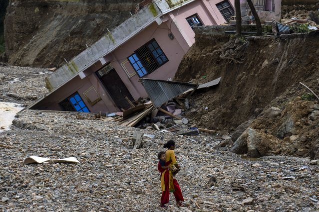 A woman with a child on her back walks past a house which had collapsed due to flooding in the Nakhu river caused by heavy rains in Lalitpur, Nepal, on Tuesday, October 1, 2024. (Photo by Niranjan Shrestha/AP Photo)