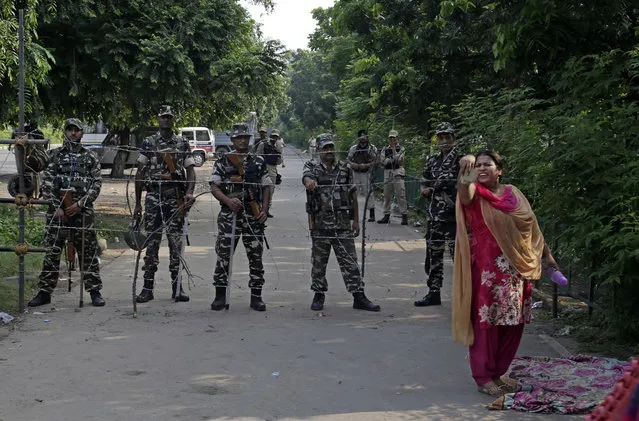 A supporter of the Dera Sacha Sauda religious sect squat others to join her as Indian paramilitary soldiers stand guard on a barricaded road leading to a court in Panchkula, India, Friday, August 25, 2017. (Photo by Altaf Qadri/AP Photo)