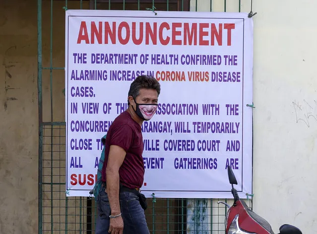 A man wearing a protective mask walks past a sign at a basketball court that announces it's temporary closure as a precautionary measure against the spread of the new coronavirus in suburban Quezon city, Manila, Philipines on Saturday March 14, 2020. Philippine officials on Saturday declared a night curfew in the capital and said millions of people in the densely populated region could only go out of their homes for work, buy necessities and medical emergencies at daytime under a monthlong quarantine to be imposed to fight the new coronavirus. (Photo by Aaron Favila/AP Photo)