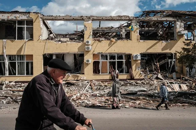 People walk past a destroyed building in Kupiansk, Kharkiv region, on September 19, 2022, amid the Russian invasion of Ukraine. In the northeastern town of Kupiansk, which was recaptured by Ukrainian forces, clashes continued with the Russian army entrenched on the eastern side of the Oskil river. (Photo by Yasuyoshi Chiba/AFP Photo)