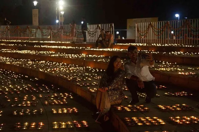 People pose for a selfie sitting by lamps lit to celebrate Diwali festival during the “Diye Jalao, Patakhe Nahi” or “light lamps not firecrackers”, event in New Delhi, India, Friday, October 21, 2022. (Photo by Bhumika Saraswati/AP Photo)