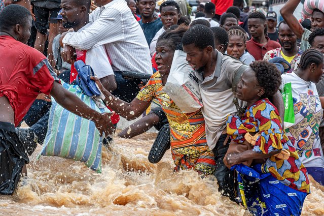 A man assists two women as residents wade through murky floodwaters following heavy rains in the Ndjili district of Kinshasa on April 6, 2025. Heavy downpours in the Democratic Republic of Congo's capital Kinshasa have left around 30 people dead while wrecking havoc in the central African megacity, an official told AFP on April 6, 2025. After the rain poured down overnight from Friday to Saturday, the rising water levels devastated several outlying and impoverished suburbs of the metropolis of some 17 million people. (Photo by Hardy Bope/AFP Photo)