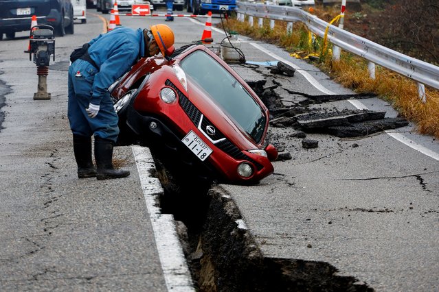 A worker looks at a car stuck on a broken road in the aftermath of an earthquake, near Anamizu, Japan on January 3, 2024. (Photo by Kim Kyung-Hoon/Reuters)