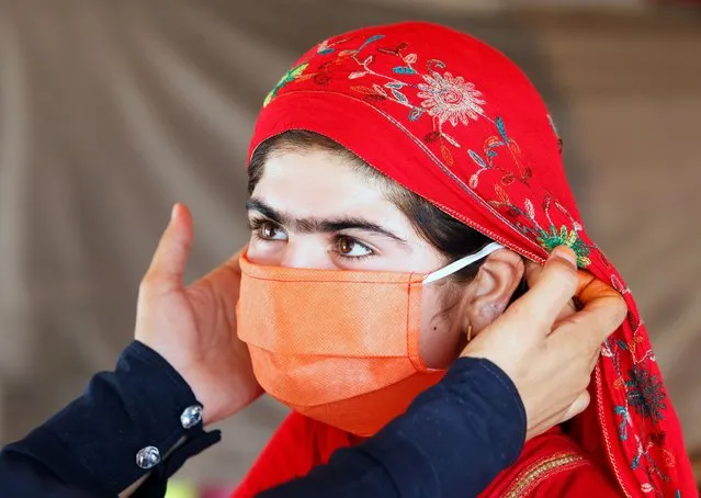 A UNICEF worker helps an internally displaced girl put on a face mask at a makeshift camp, amid the coronavirus disease (COVID-19) outbreak, in Jalalabad, Afghanistan June 22, 2020. (Photo by Reuters/Parwiz)