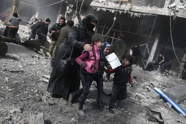 A Syrian woman and children run for cover amid the rubble of buildings following government bombing in the rebel-held town of Hamouria, in the besieged Eastern Ghouta region on the outskirts of the capital Damascus, on February 19, 2018. Heavy Syrian bombardment killed 44 civilians in rebel-held Eastern Ghouta, as regime forces appeared to prepare for an imminent ground assault. (Photo by Abdulmonam Eassa/AFP Photo)