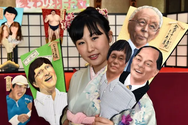 Japanese doll maker Kyugetsu employee Saeko Koyama, wearing a kimono dress, displays an ornamental wooden racket or “hagoita” decorated with a depiction of three Japanese Nobel laureate scientists (R) and Mixrosoft's Bill Gates (L) at the company's showroom in Tokyo on December 3, 2014. A hagoita is a wooden paddle used to play the new year hanetsuki game, where two players hit a shuttlecock back and forth. (Photo by Yoshikazu Tsuno/AFP Photo)